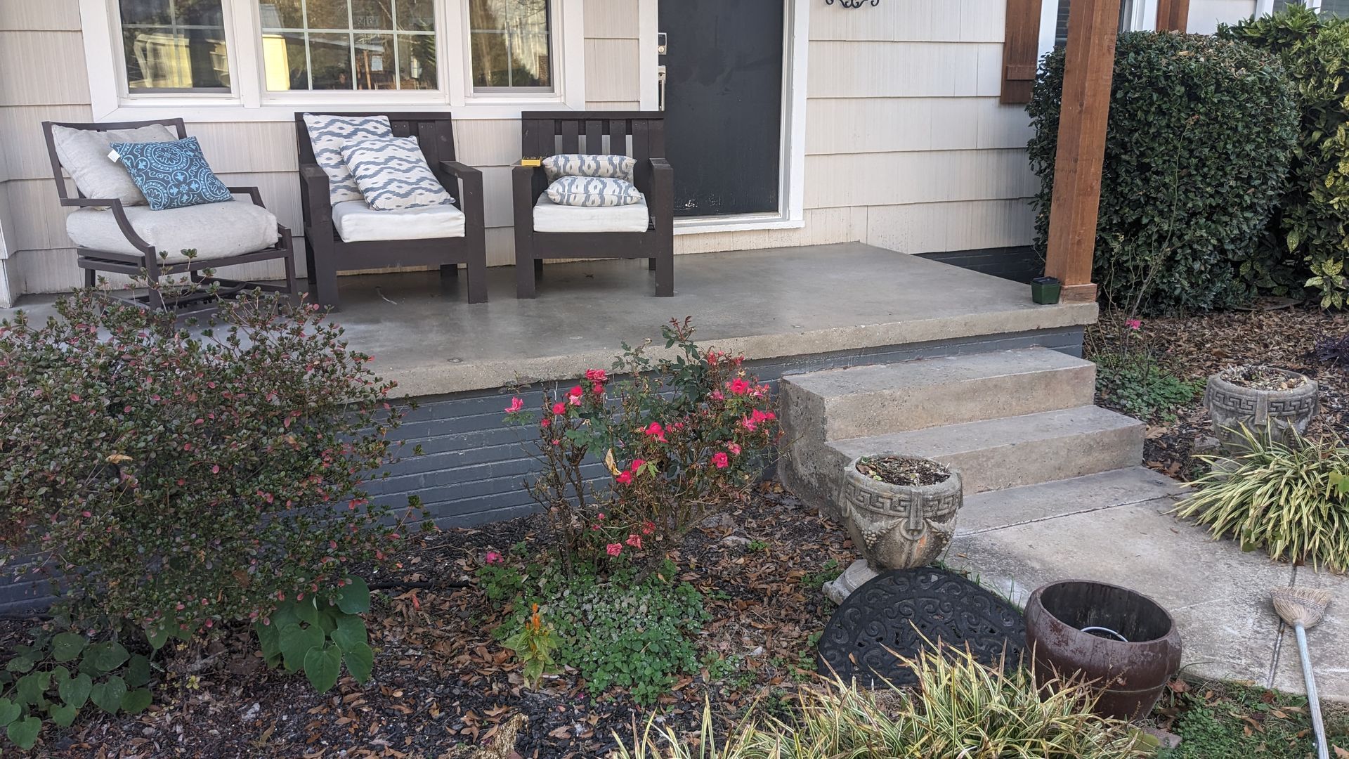 A porch with two chairs and a potted plant in front of a house.