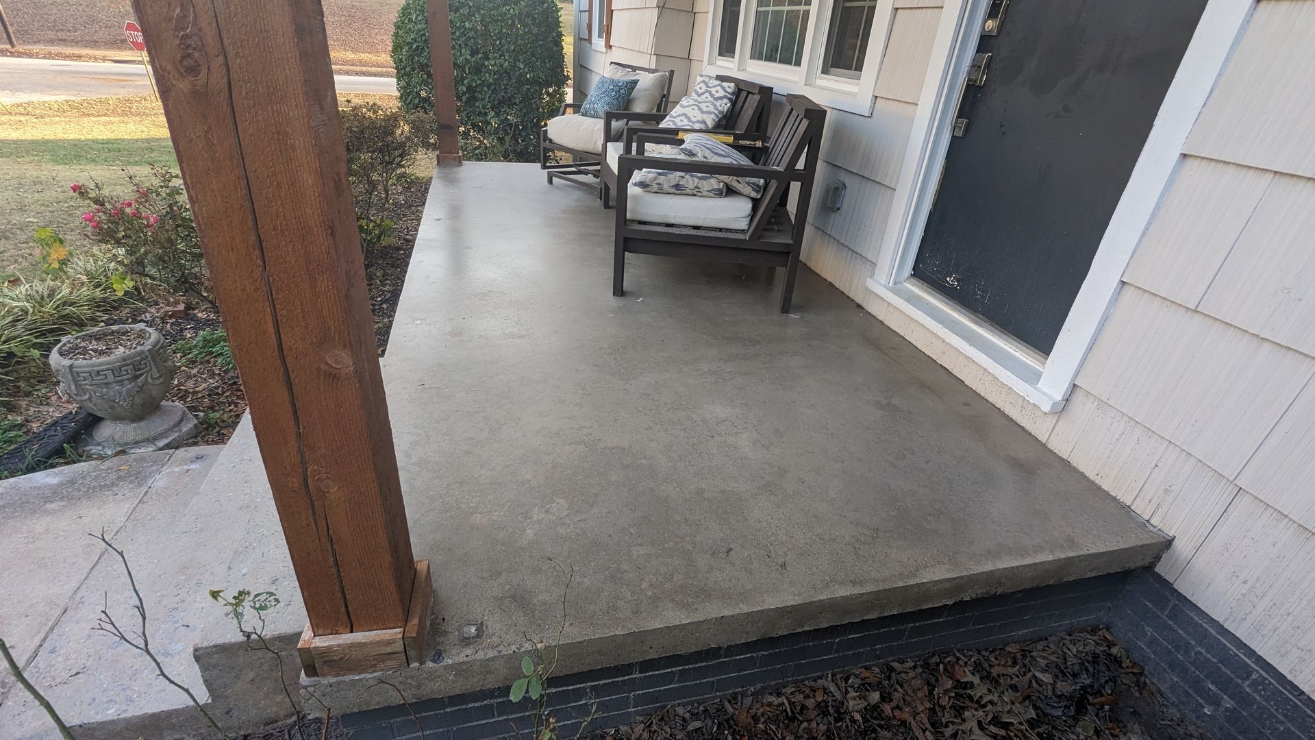 A concrete porch with chairs and a couch on it in front of a house.