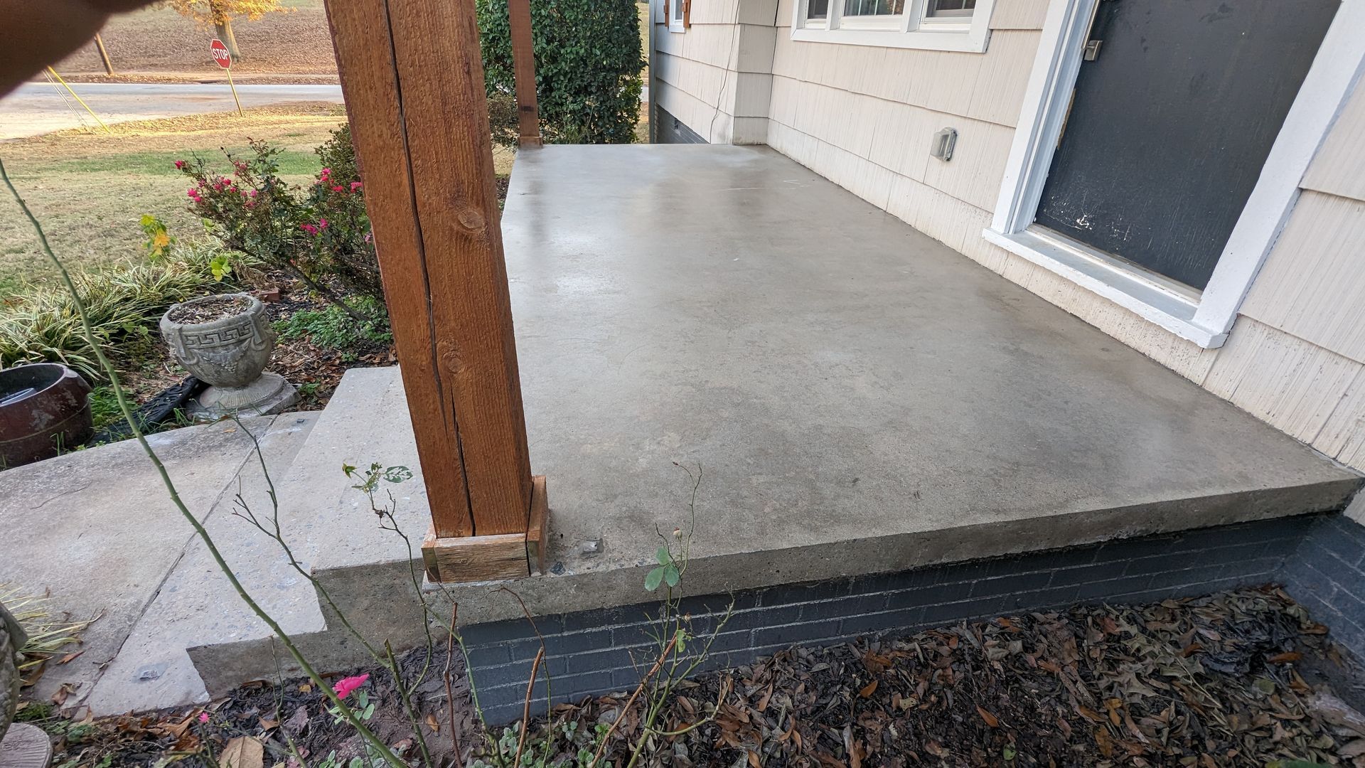 A concrete porch with a wooden railing and steps next to a house.