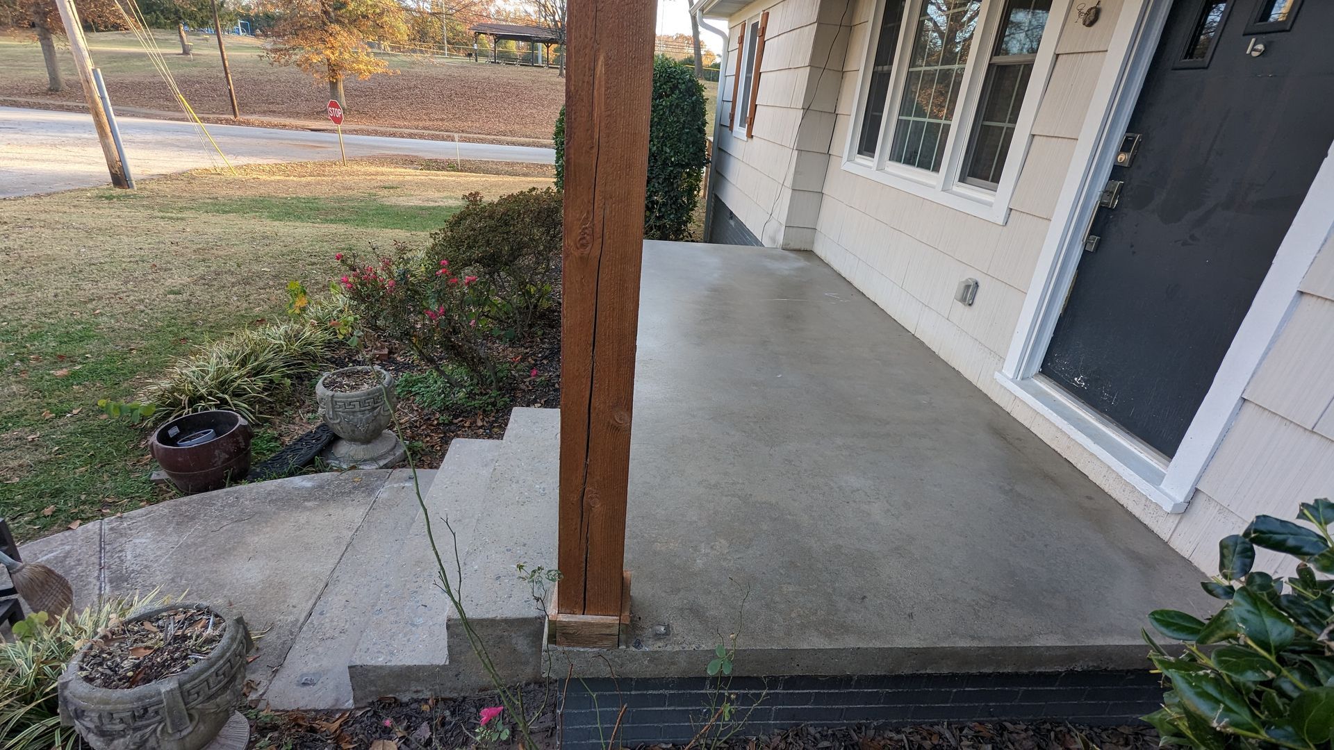 A concrete porch with a wooden post and steps leading to the front door of a house.
