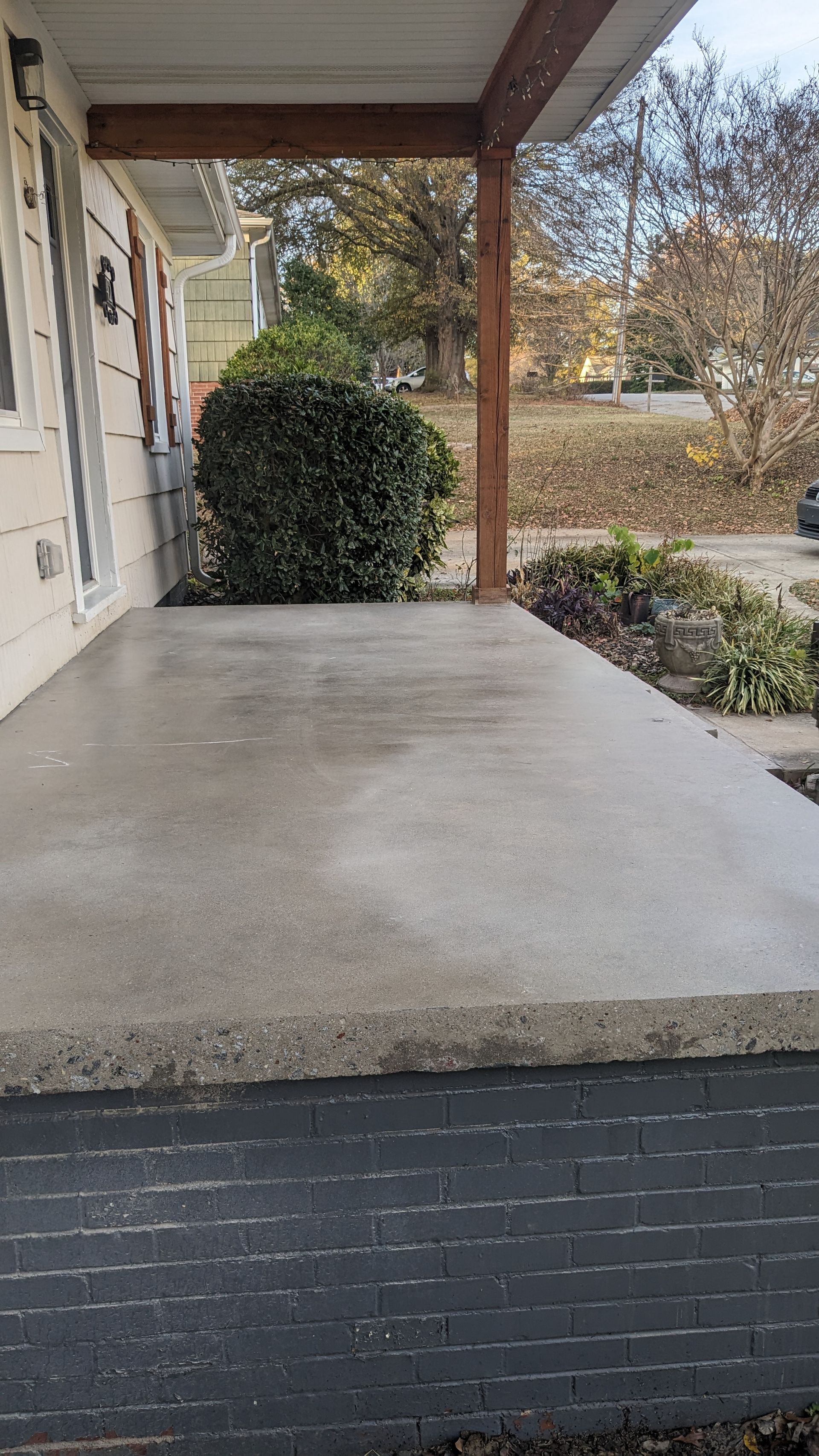 A concrete porch with a brick wall and a tree in the background.