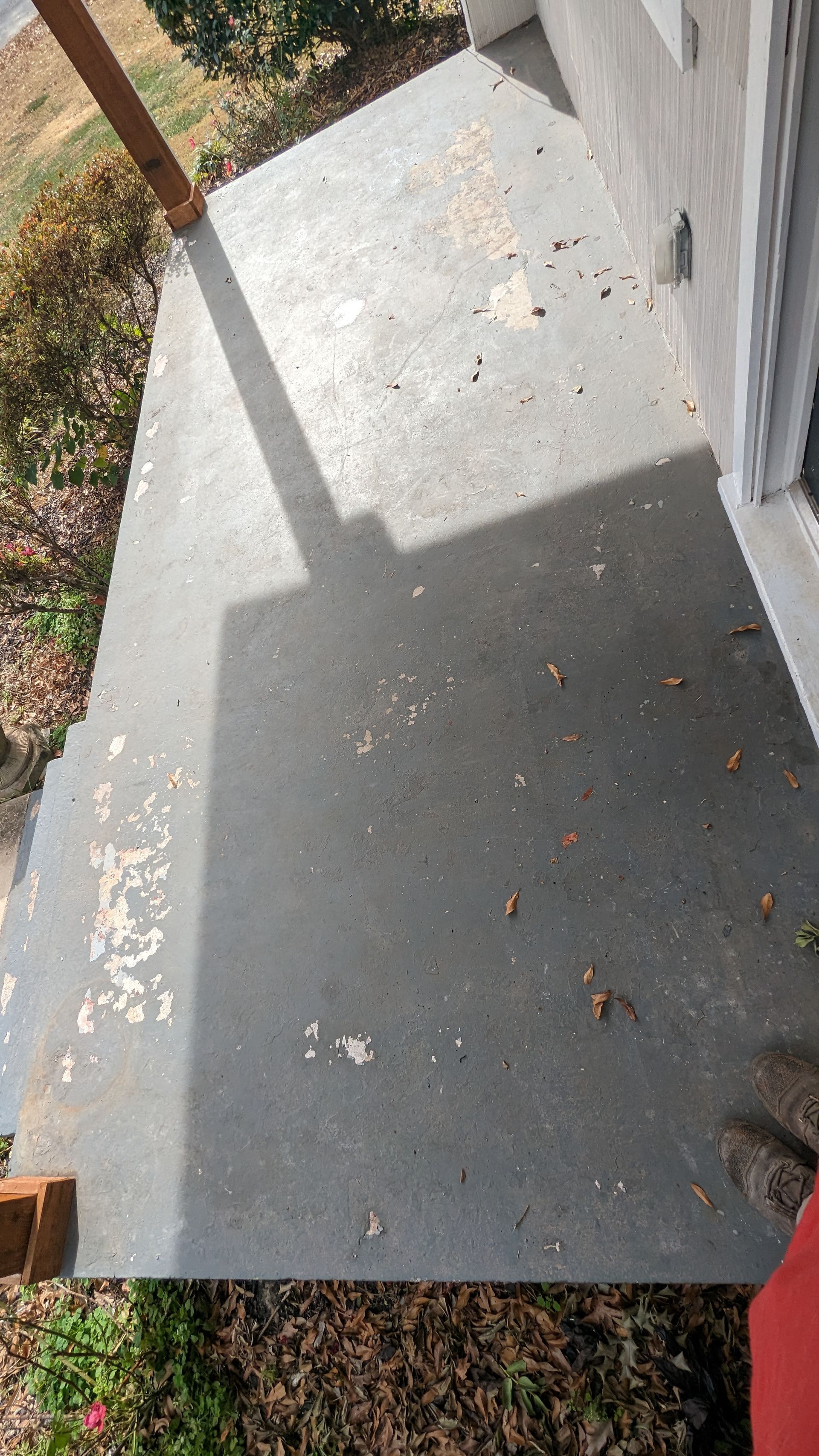A person is standing on a dirty porch next to a house.