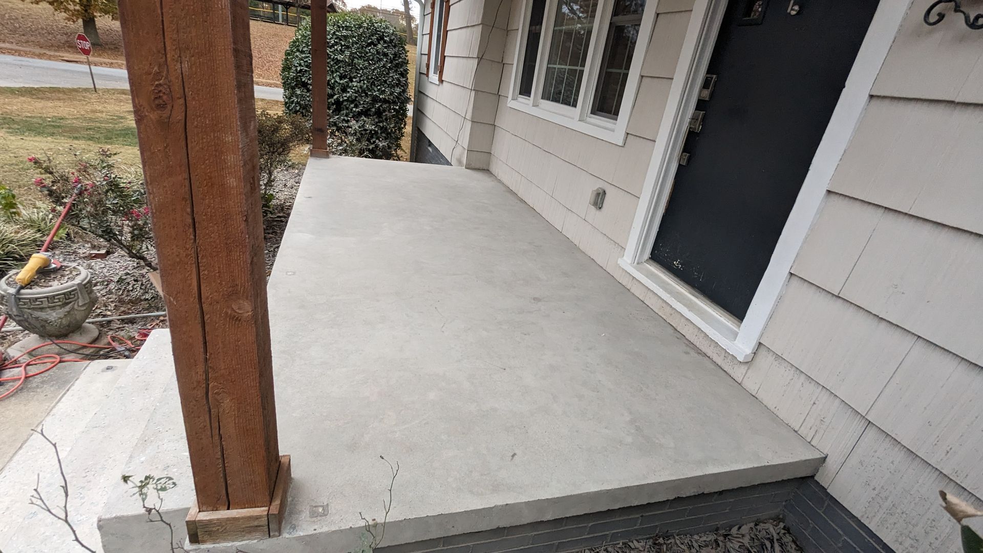 A concrete porch with a wooden pillar in front of a house.