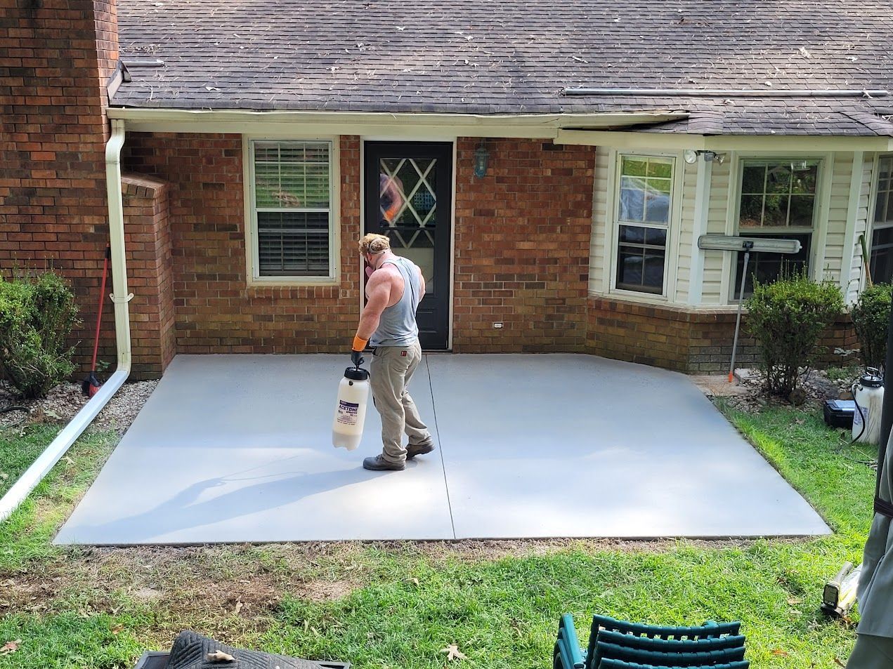 A man is painting a concrete patio in front of a brick house.
