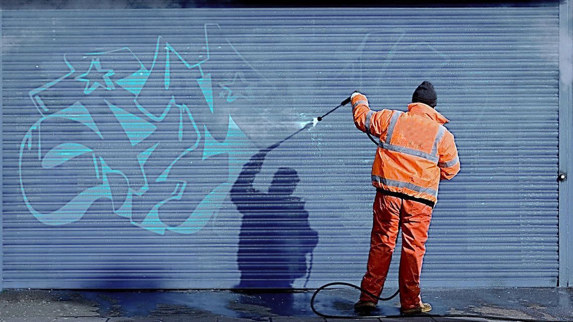 A man is cleaning graffiti on a garage door with a high pressure washer.
