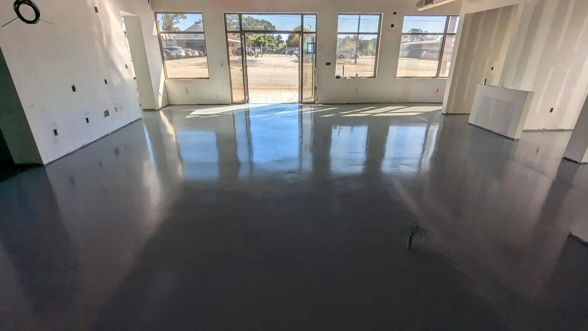 Glossy dark gray epoxy concrete floor in a commercial space with large windows and unfinished white 