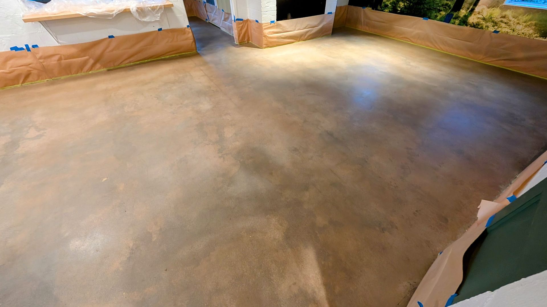 Polished concrete floor in a room, with brown tones and protective paper on the walls.