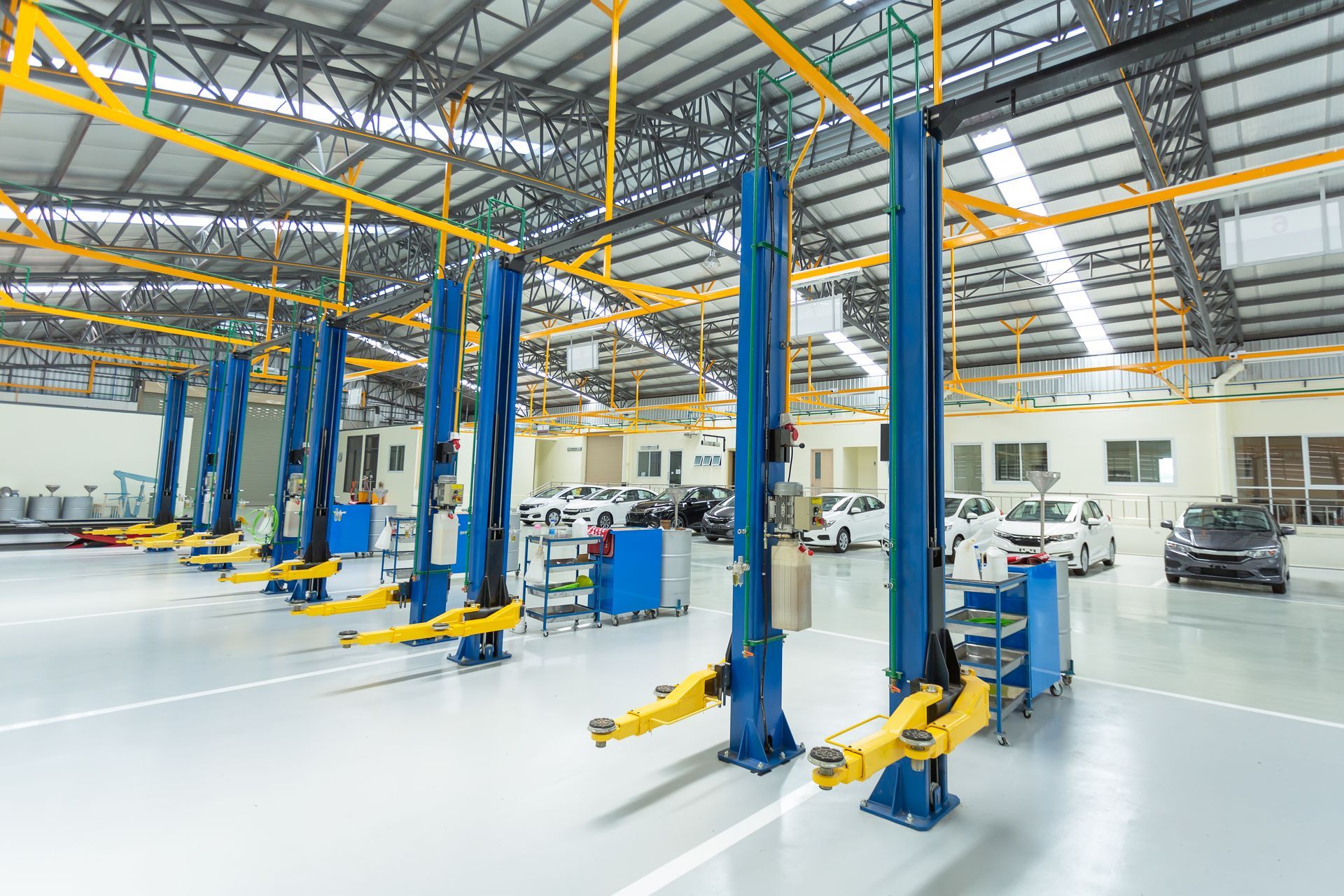 A row of blue and yellow lifts in a garage with cars parked in the background.