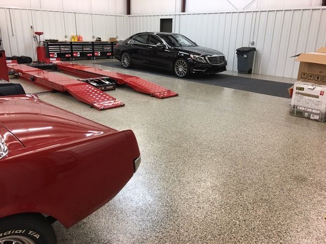 A black car is parked in a garage next to a red car.