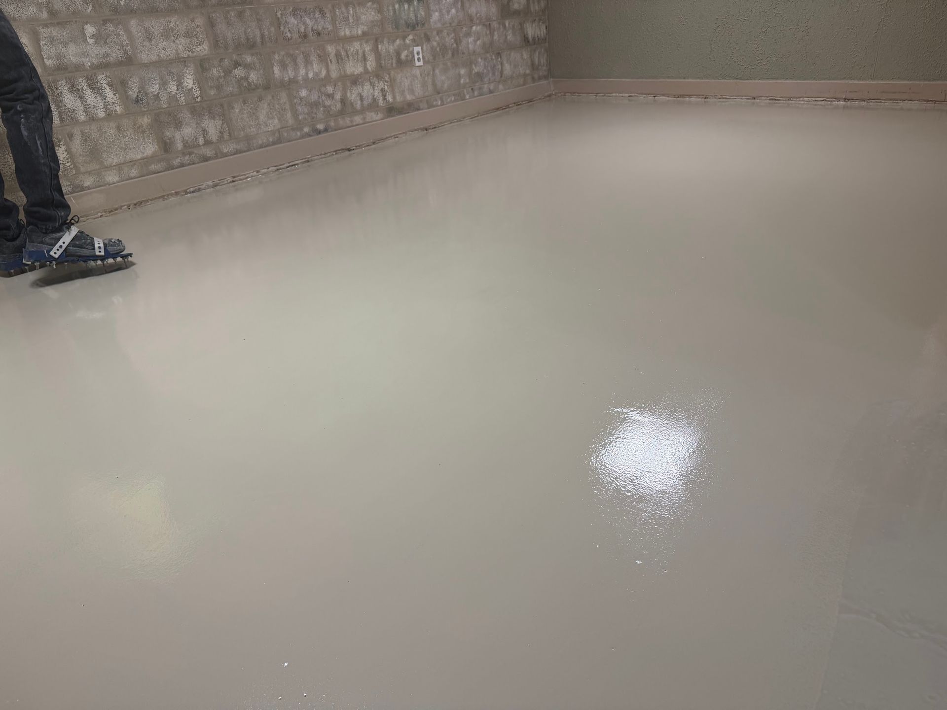 Glossy dark gray epoxy concrete floor in a commercial space with large windows and unfinished white 