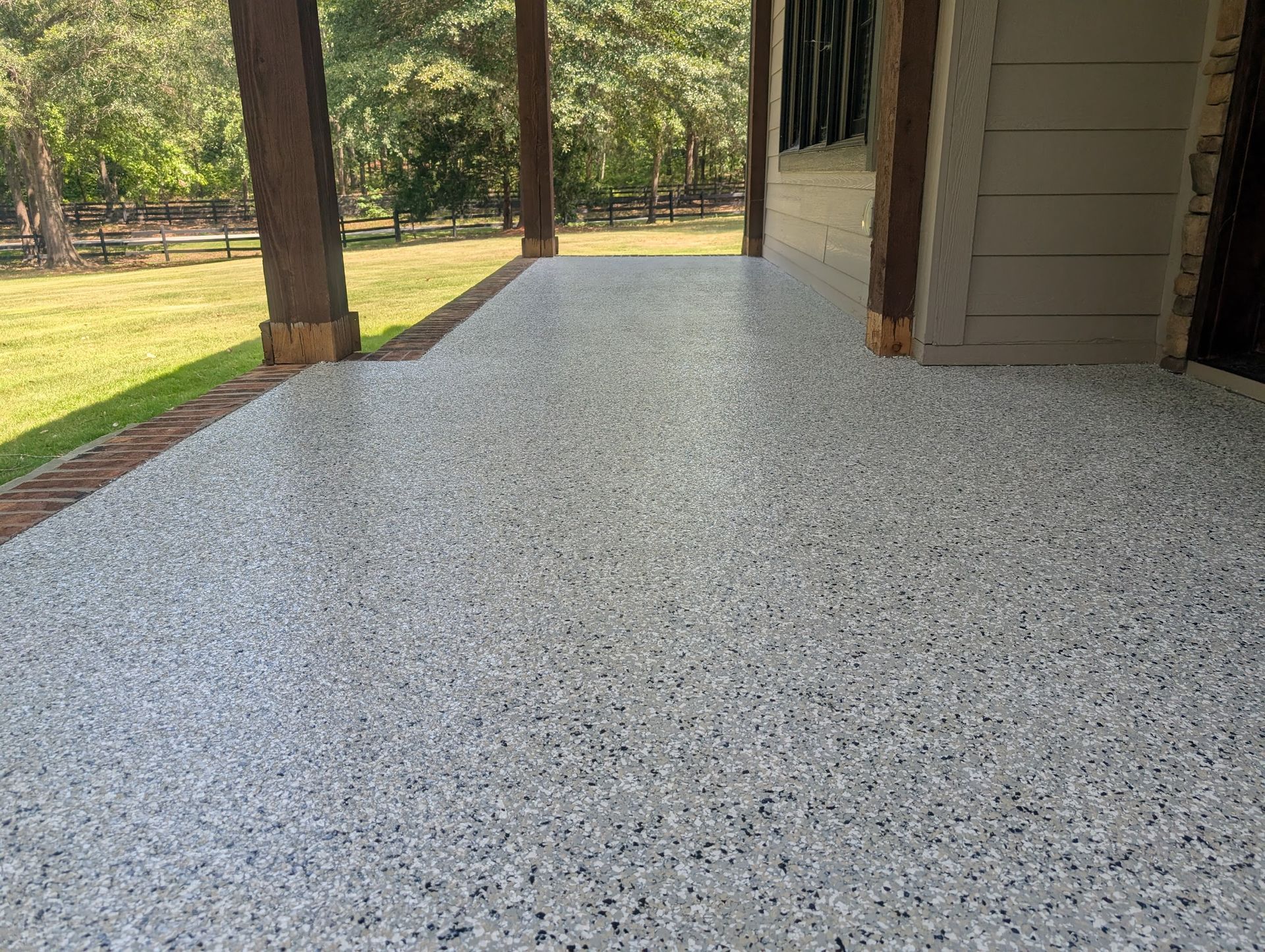 Epoxy-coated patio with speckled finish under covered porch, surrounded by greenery in Greenville