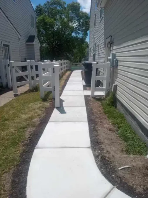 A concrete walkway between two houses with a white fence.