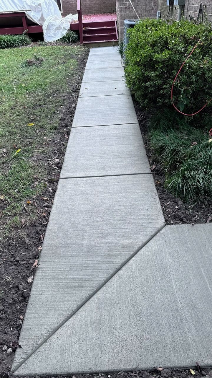 A concrete sidewalk leading to a house with stairs.