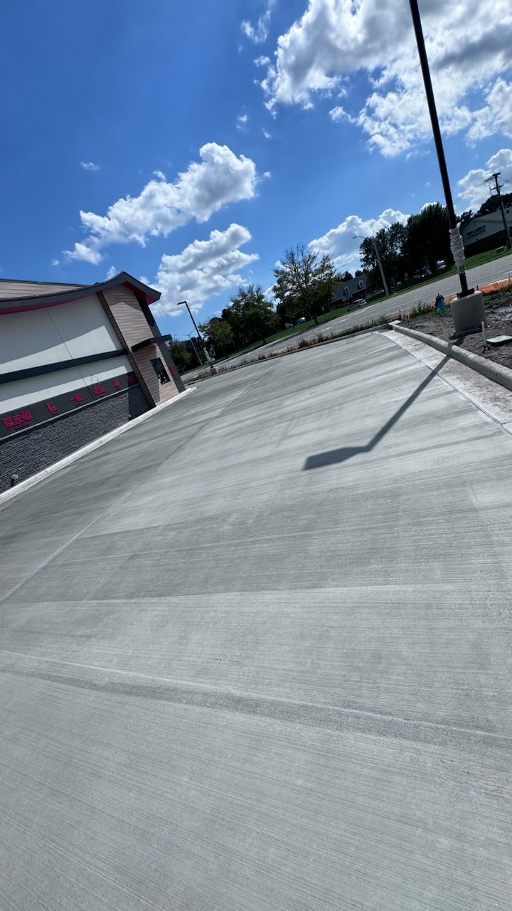 A concrete driveway with a building in the background and a blue sky with clouds.