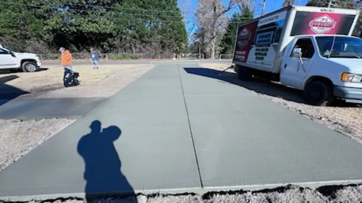 A truck is parked on the side of the road next to a concrete driveway.