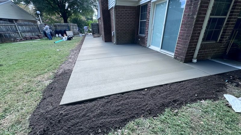 A concrete walkway is being built in the backyard of a brick house.