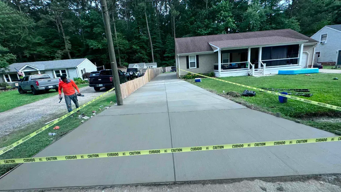 A man is walking down a concrete driveway in front of a house.