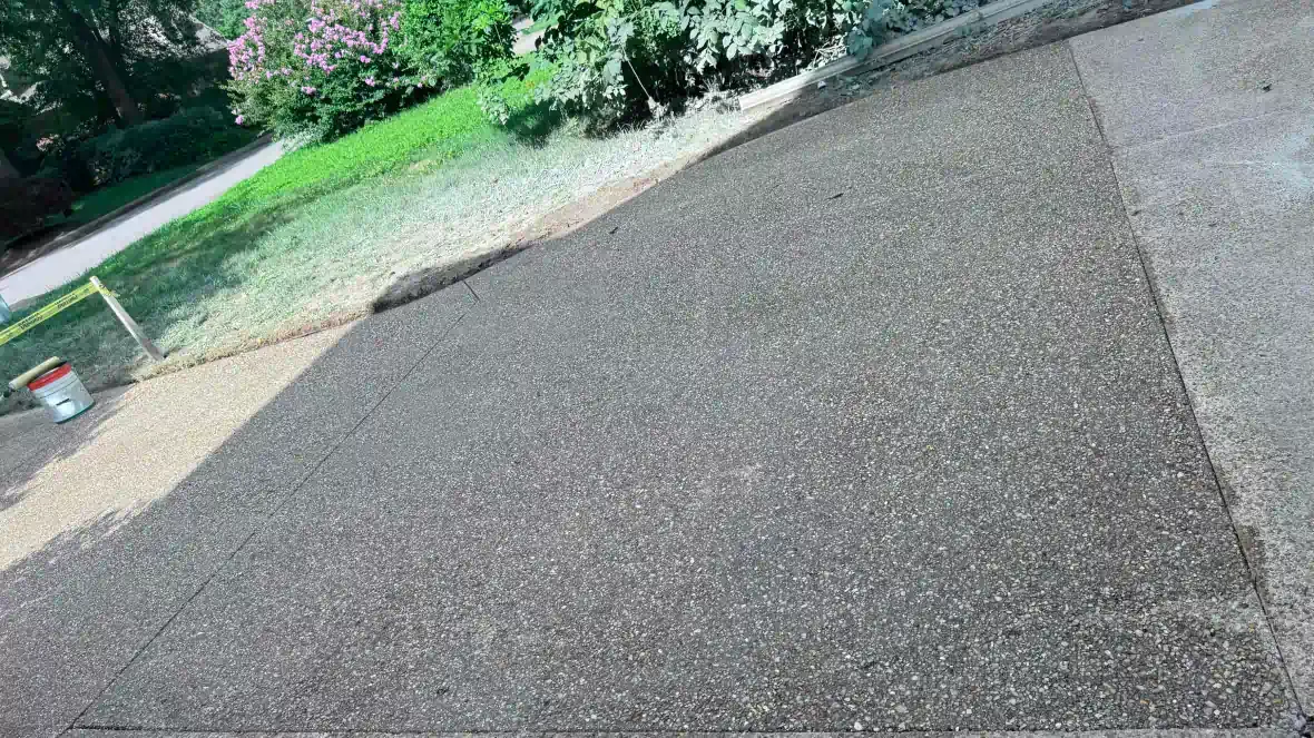 A close up of a concrete driveway with a bucket in the background.