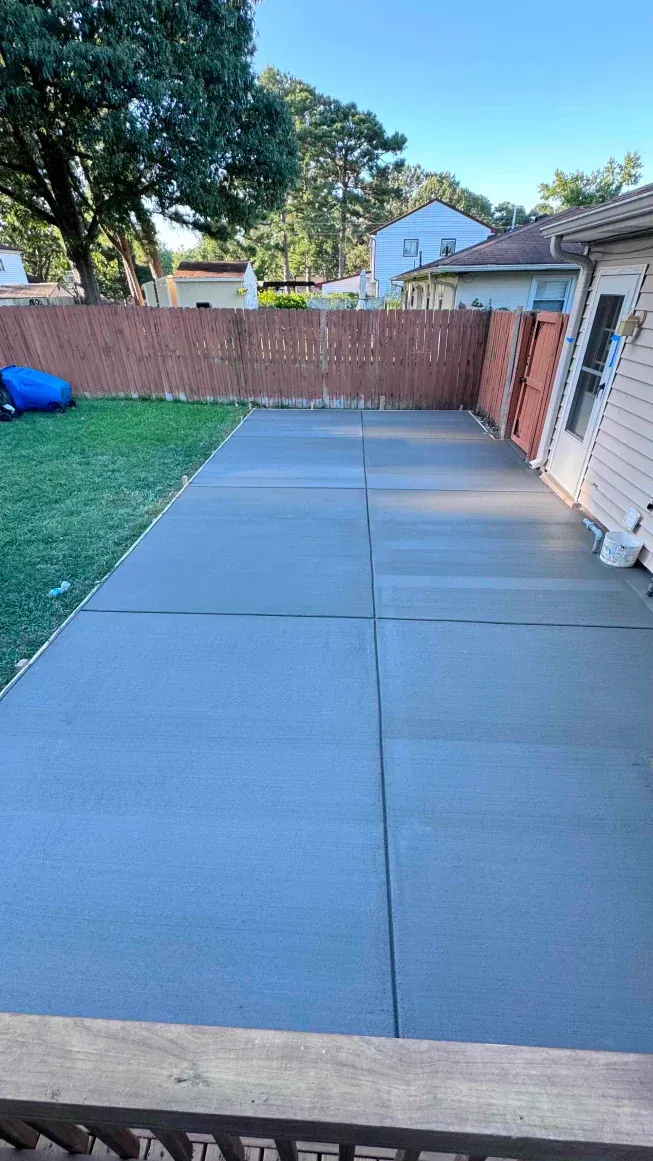 A concrete patio with a fence in the backyard of a house.