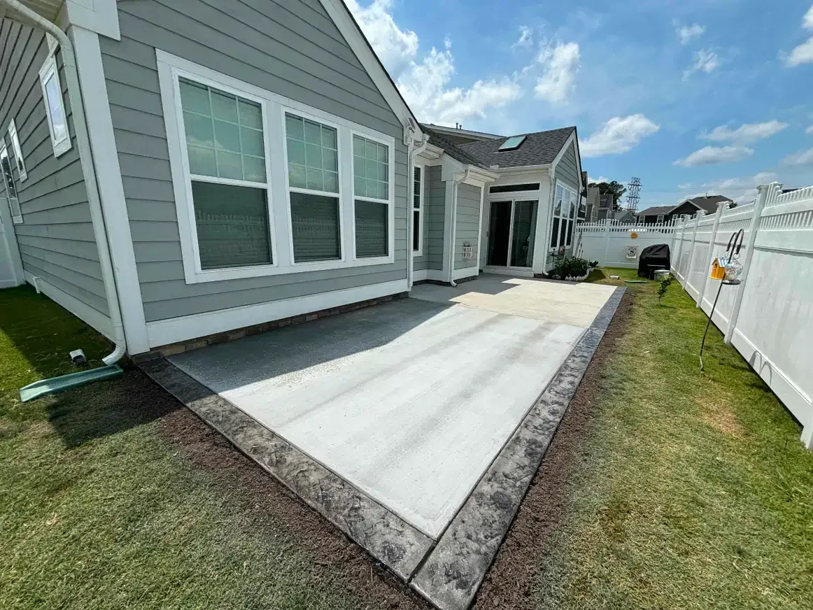 The backyard of a house with a concrete patio and a white fence.