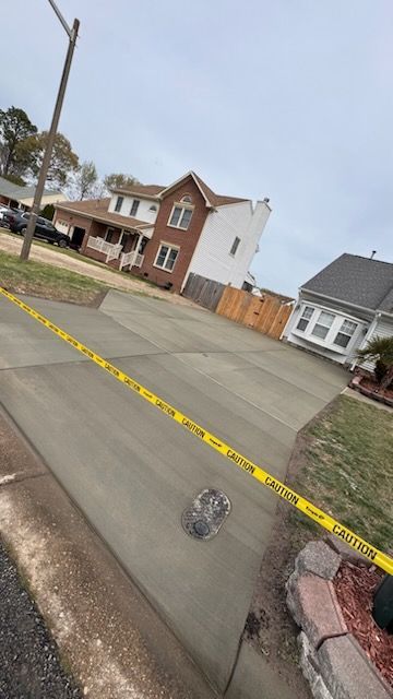 A concrete driveway with a yellow caution tape around it and a house in the background.