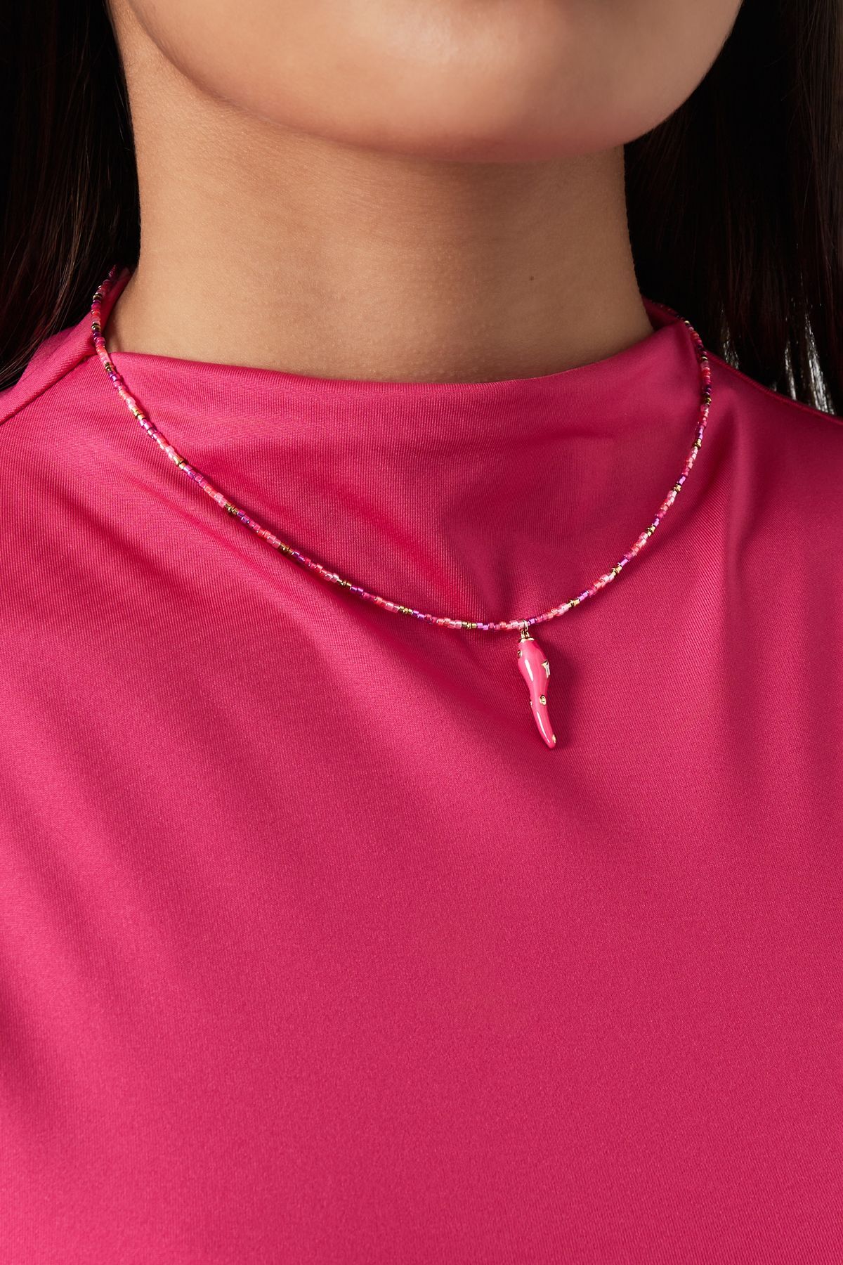 Een roze kralenketting met een klein, bijpassend bedeltje in de vorm van een hete peper.