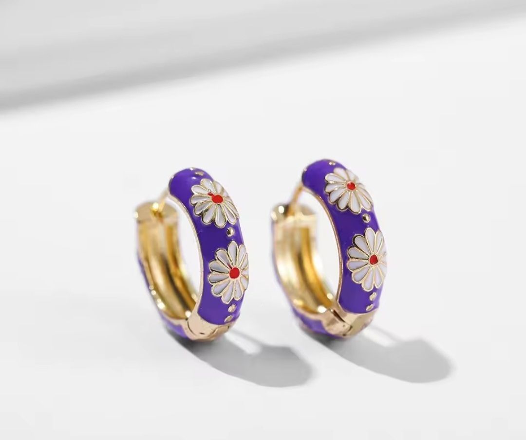 Een paar kleine gouden oorringen met een levendige paarse emaille coating, versierd met witte madeliefjes.