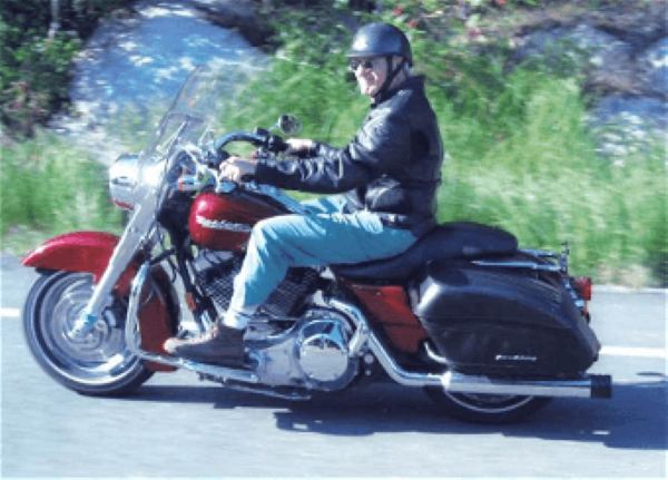 Person riding a red Harley-Davidson motorcycle on a road; wearing a helmet, jacket, and light blue pants.