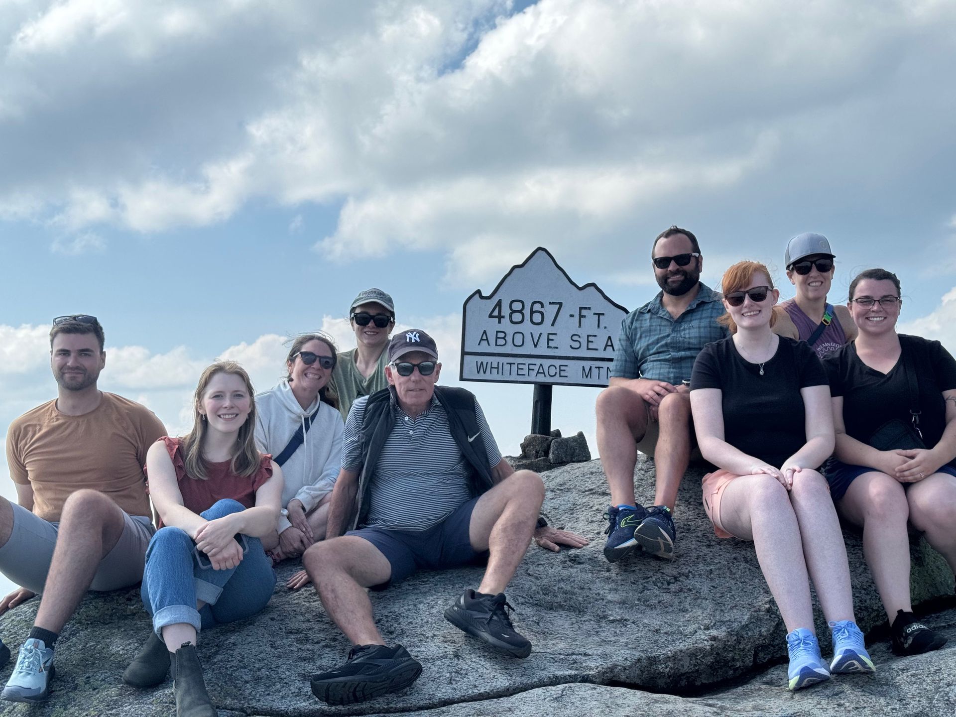 Group of people atop a mountain summit, posing by a sign that reads 