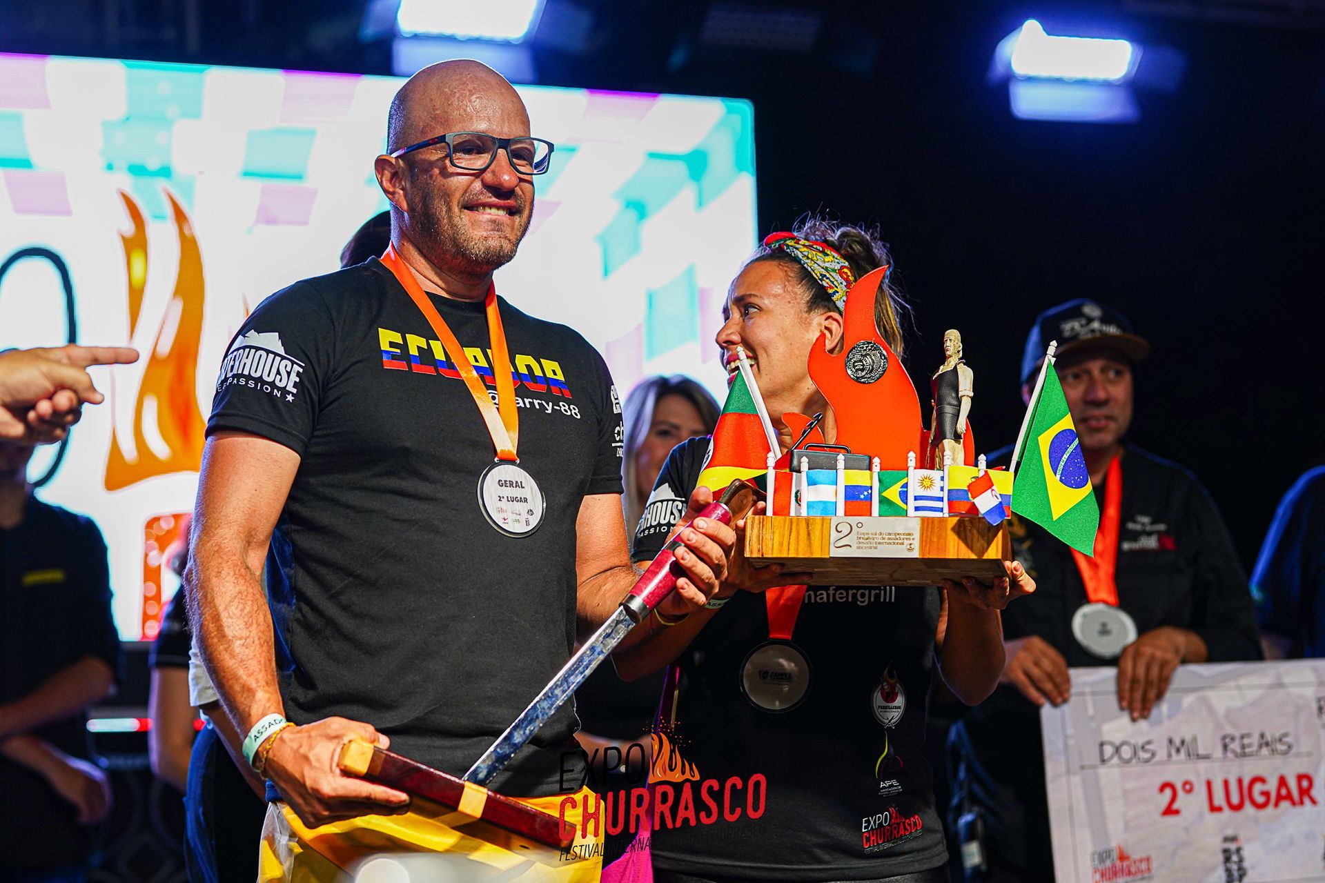 Um homem e uma mulher estão em um palco segurando um troféu.