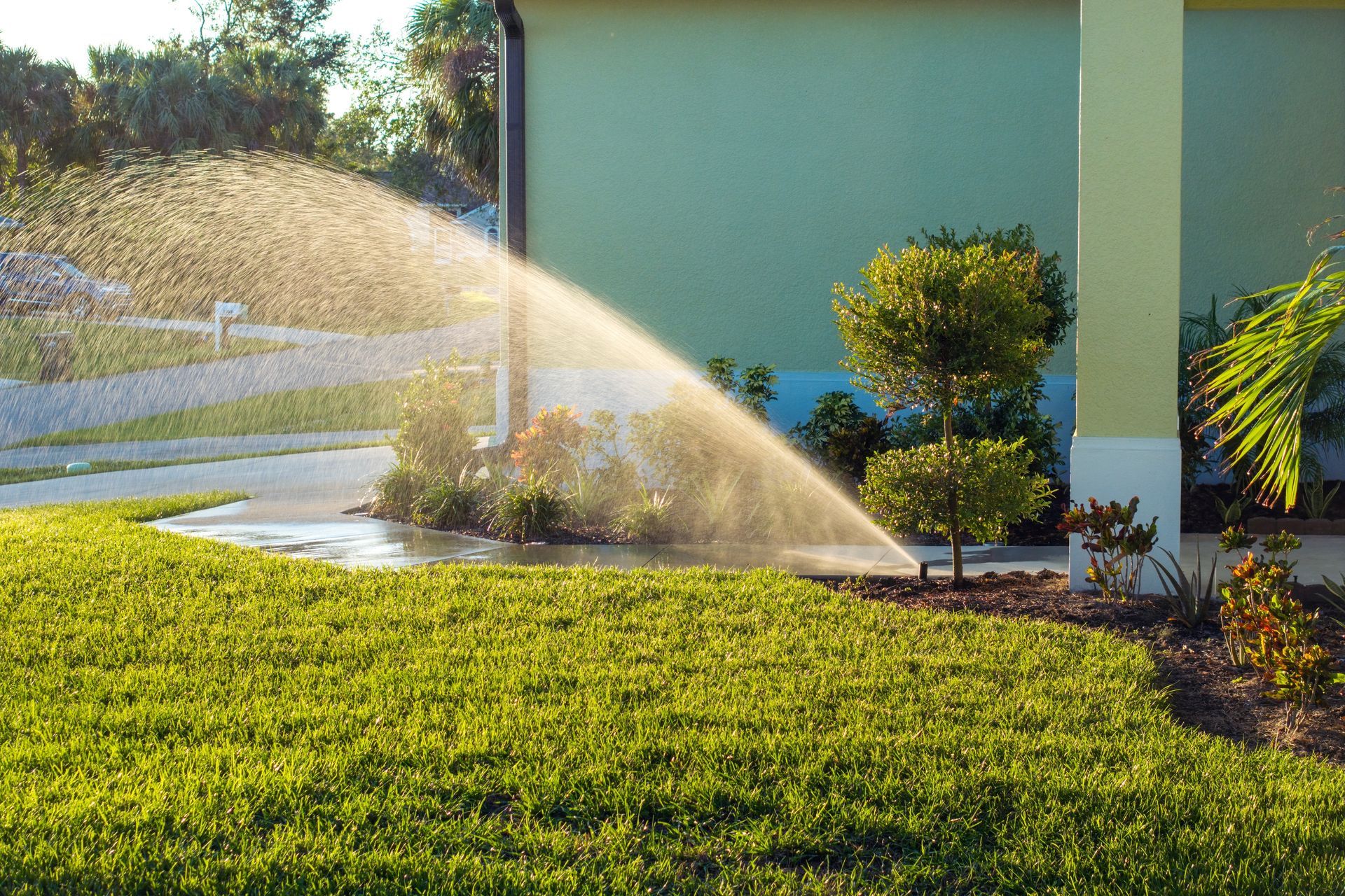 Lawn sprinkler watering green grass beside a house in bright sunlight