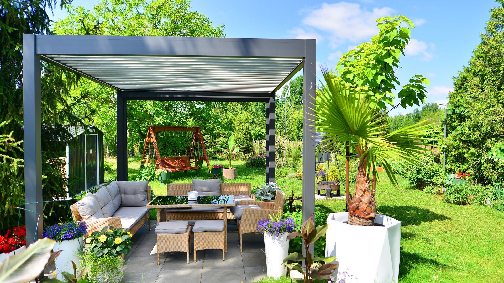 Outdoor patio with gray pergola, seating area, and lush green garden.