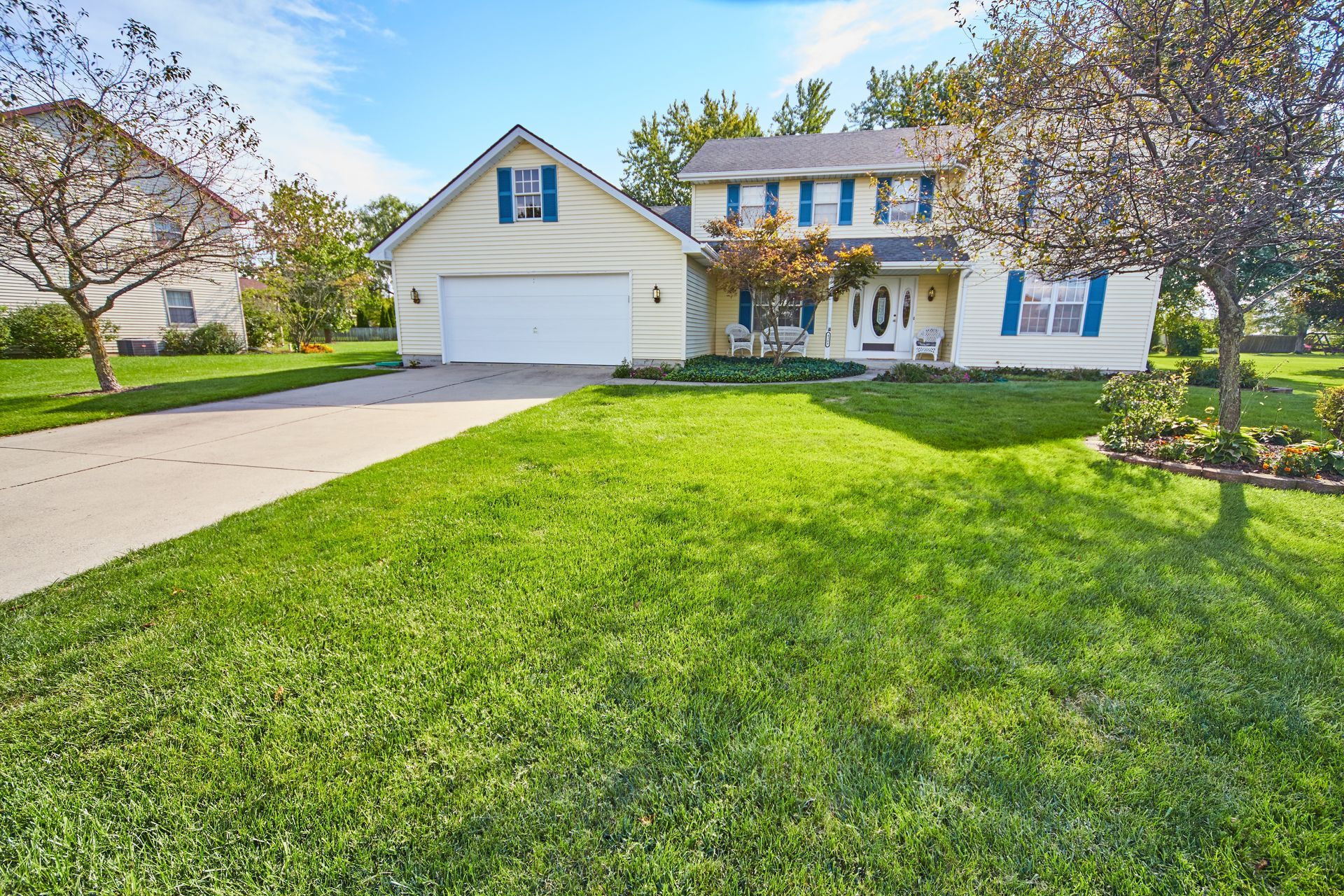 Yellow two-story house with blue shutters, a green lawn, and a driveway.