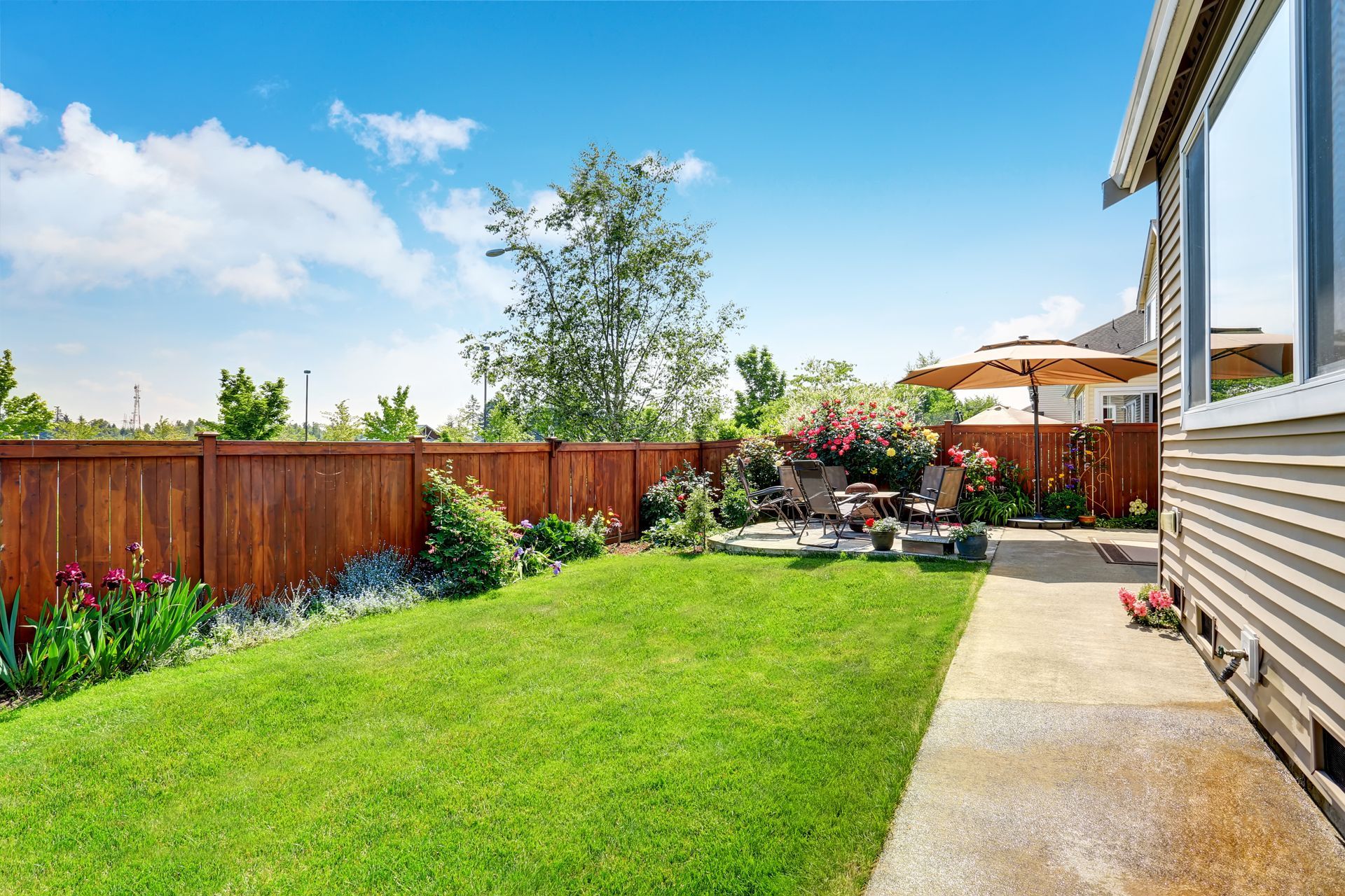 A lush green backyard with a wooden fence and a patio.