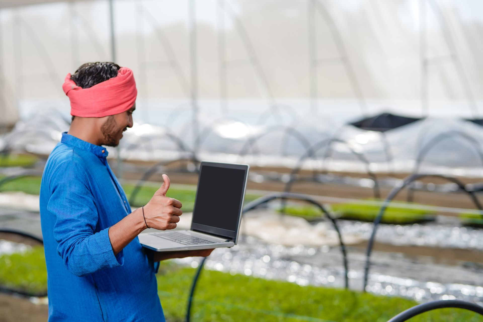 A man is holding a laptop and giving a thumbs up.