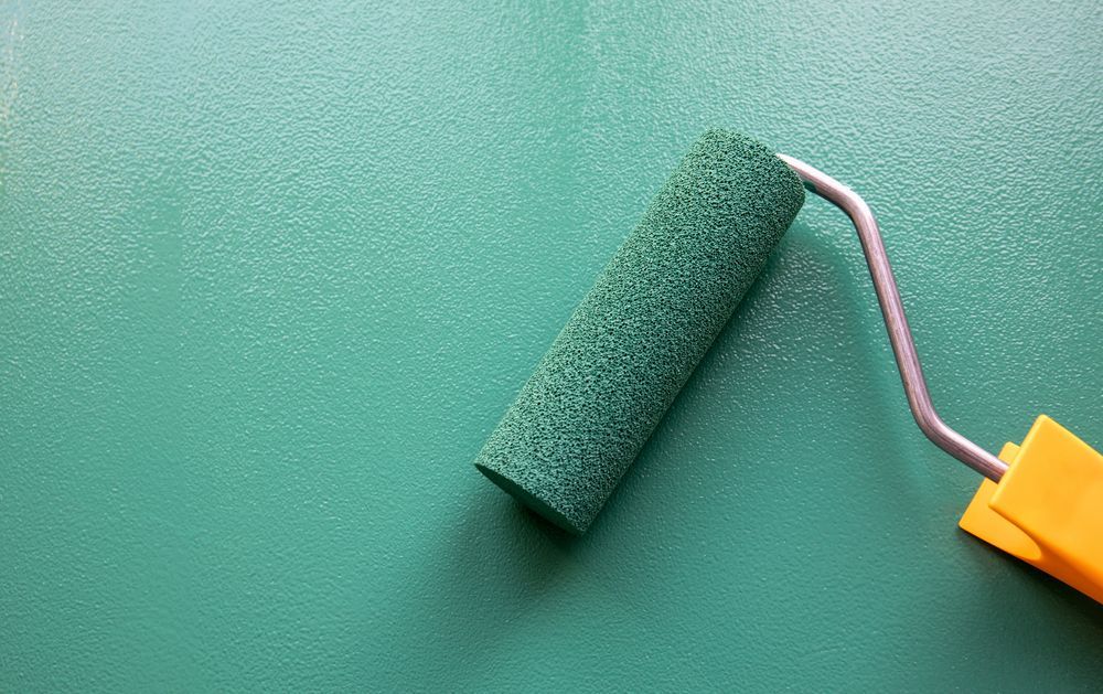 A green paint roller is sitting on a green wall.