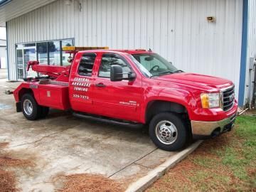 Red tow truck parked in front of a white building with the company name 