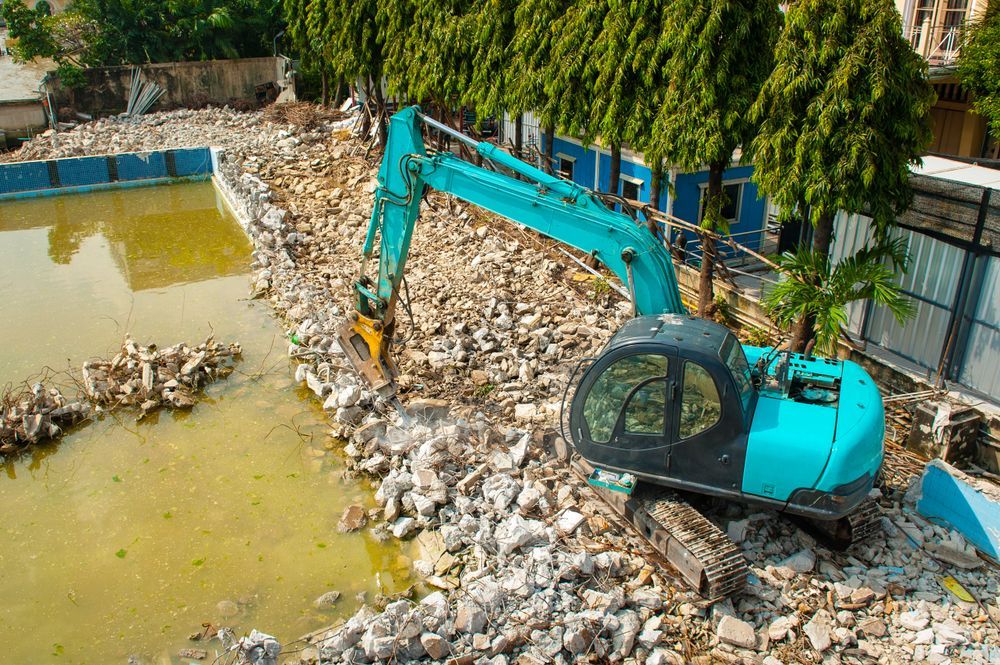 Blue Excavator Demolishing a Pool, Surrounded by Debris — AGM HIRE NQ in Kelso, QLD