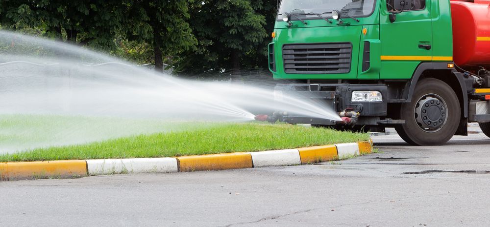 A Green Truck Spraying Water on Grass Near a Curb — AGM HIRE NQ in Kirwan, QLD