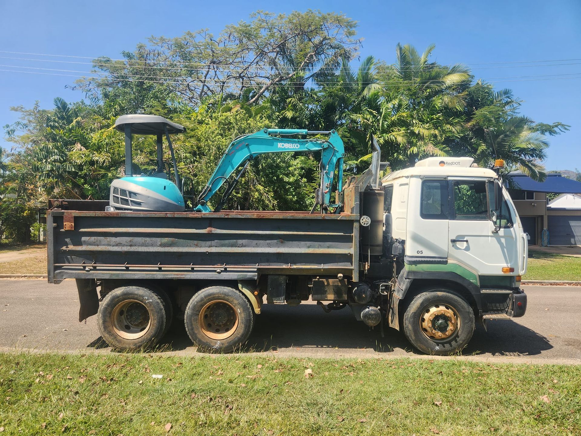 A Teal Excavator Loaded on the Back of a White and Black Dump Truck — AGM HIRE NQ in Condon, QLD