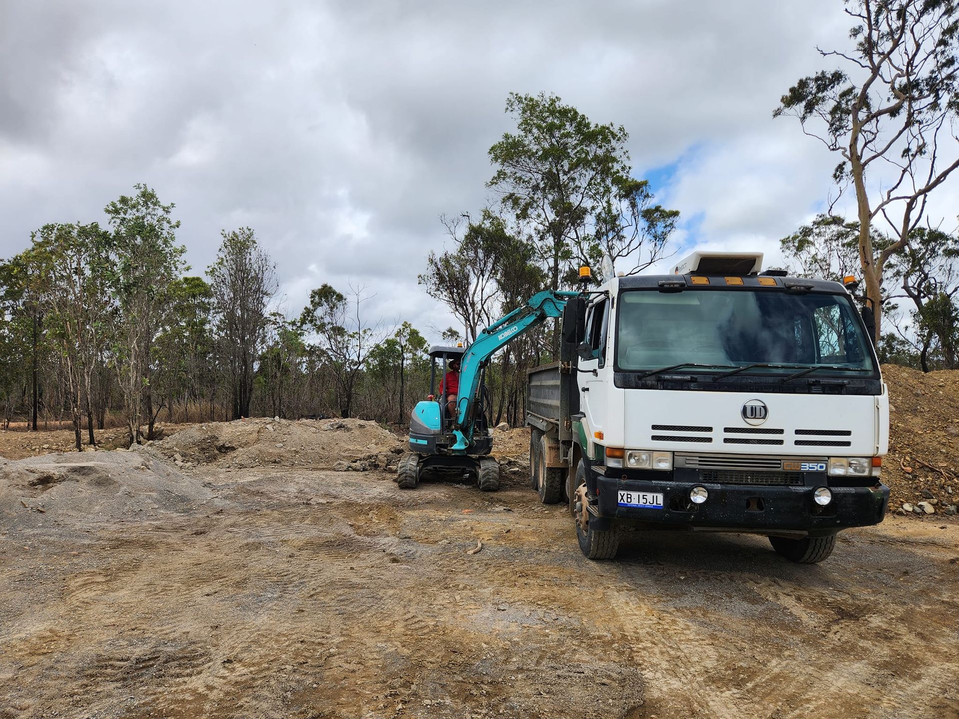 An Excavator Loading a White Truck With Gravel on a Dirt Lot — AGM HIRE NQ in Kelso, QLD