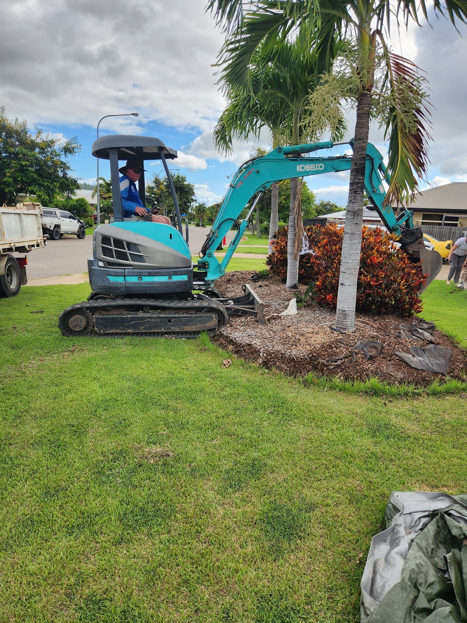 A Teal Excavator Digging in a Front Yard — AGM HIRE NQ in Condon, QLD