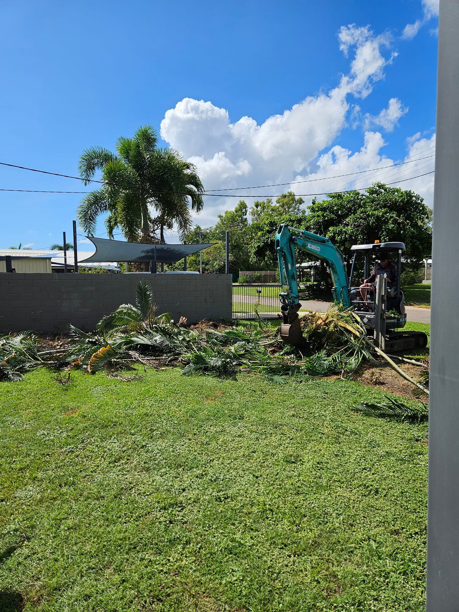 A Small Excavator Clearing Debris Beside a Concrete Wall — AGM HIRE NQ in Kirwan, QLD