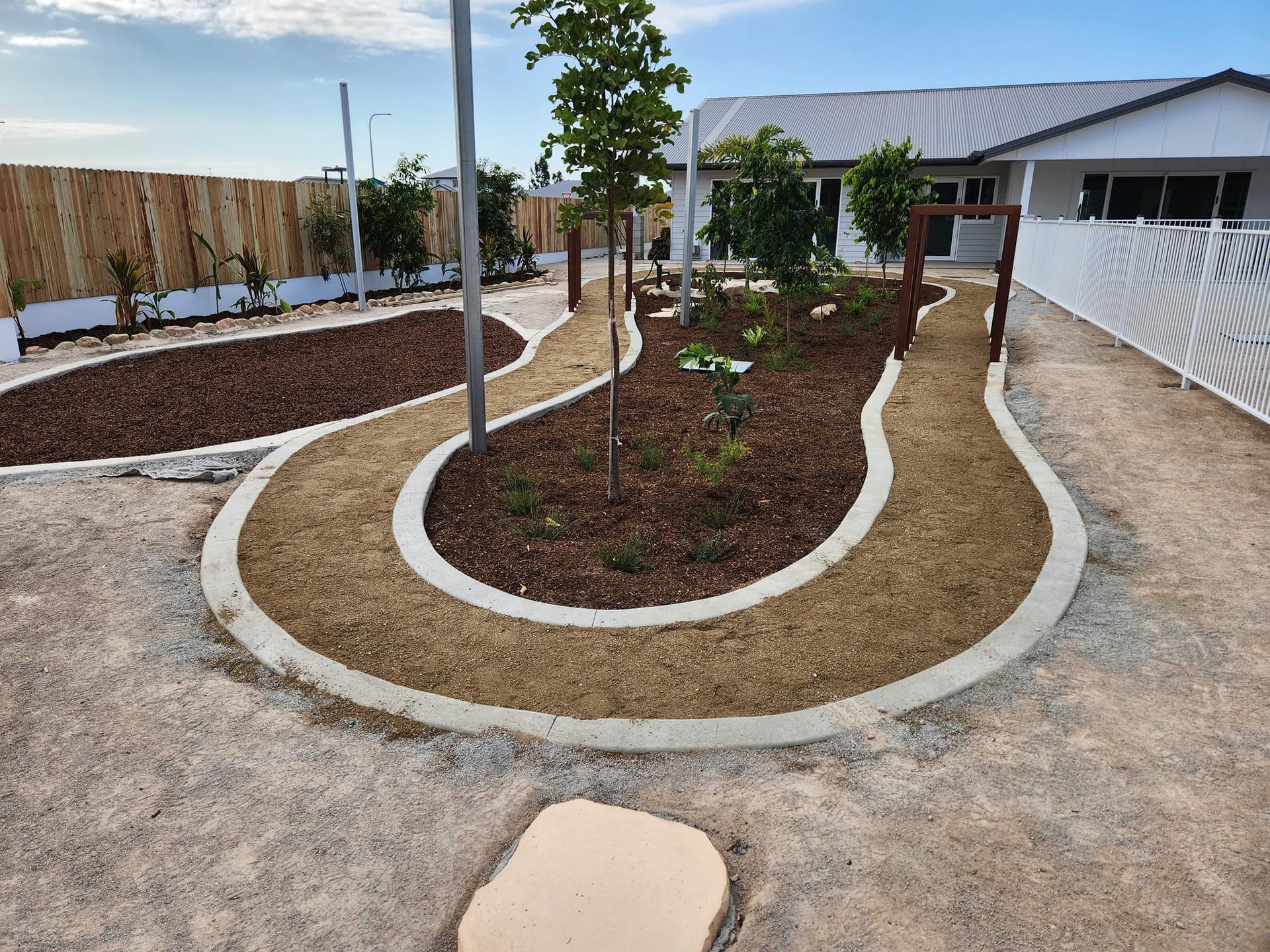 A Landscaped Garden With Curved Paths and a White Building — AGM HIRE NQ in Condon, QLD