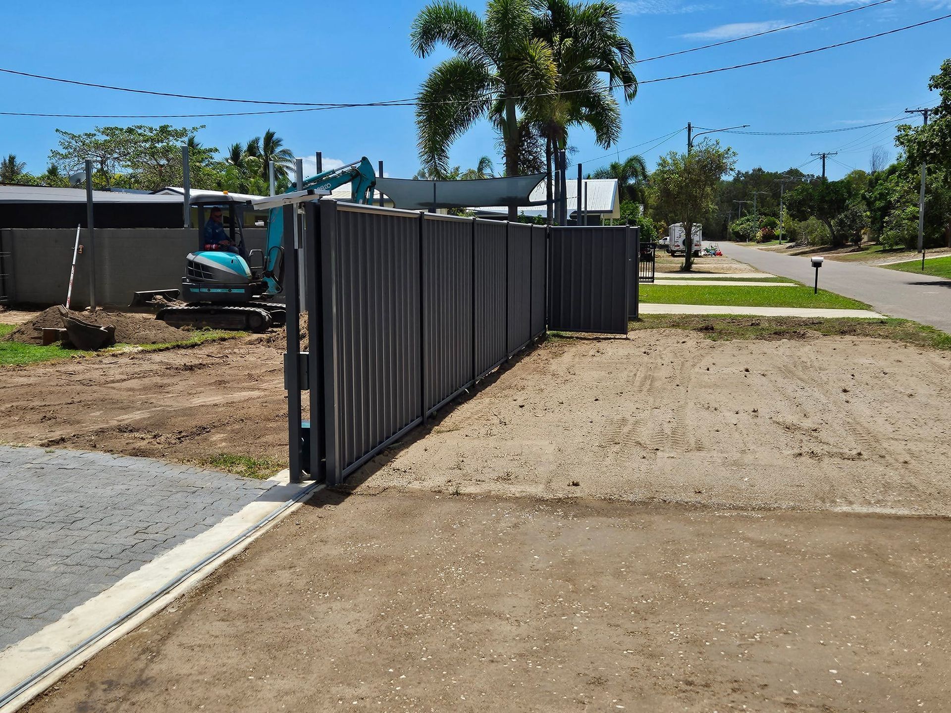 A Black Metal Fence Partially Open on a Sandy Lot, With a Small Excavator — AGM HIRE NQ in Condon, QLD