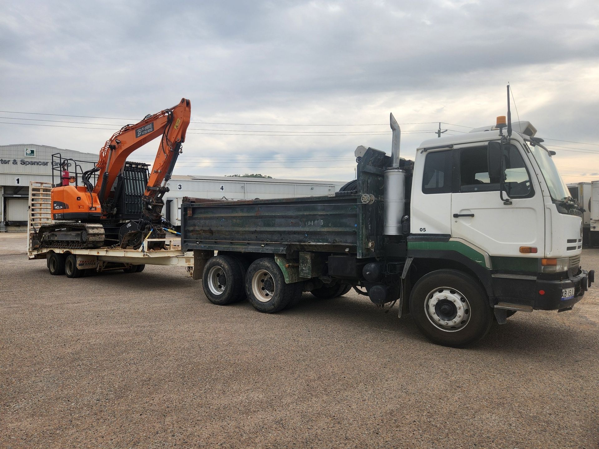 White Truck With a Green Stripe Hauling an Orange Excavator — AGM HIRE NQ in Kirwan, QLD