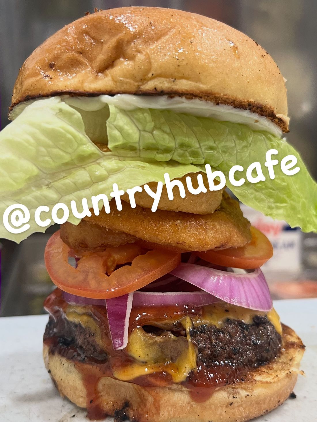 Tall cheeseburger with lettuce, tomato, onion, and sauce on a white background