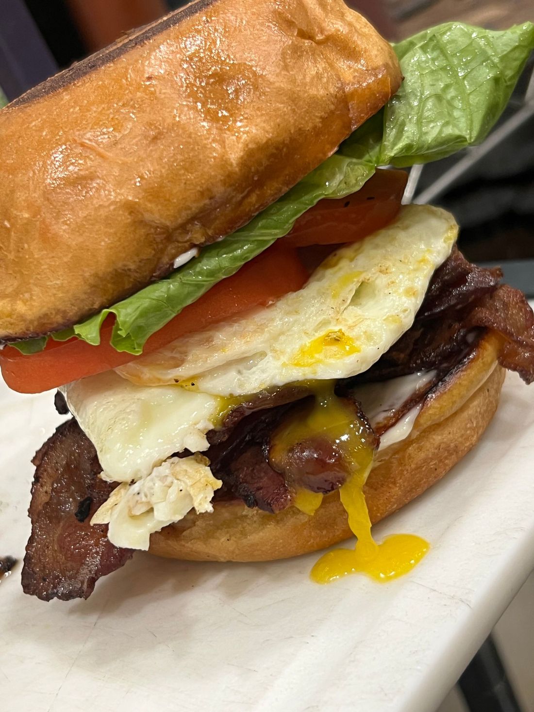 Stacked breakfast sandwich with fried egg, bacon, tomato, and lettuce on a white plate