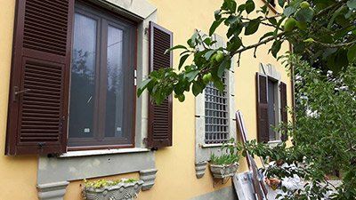 Un edificio giallo con le persiane marroni e un albero di fronte.