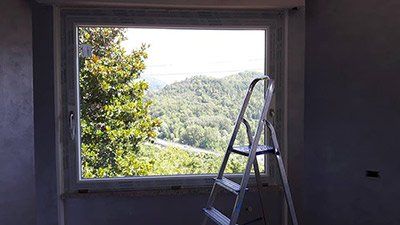 Una scala è appoggiata davanti a una finestra con vista sulla foresta.